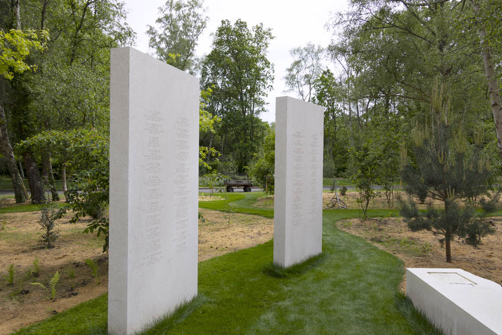 Two memorial stelae next to a Portland stone bench set on a grass path in a woodland setting.