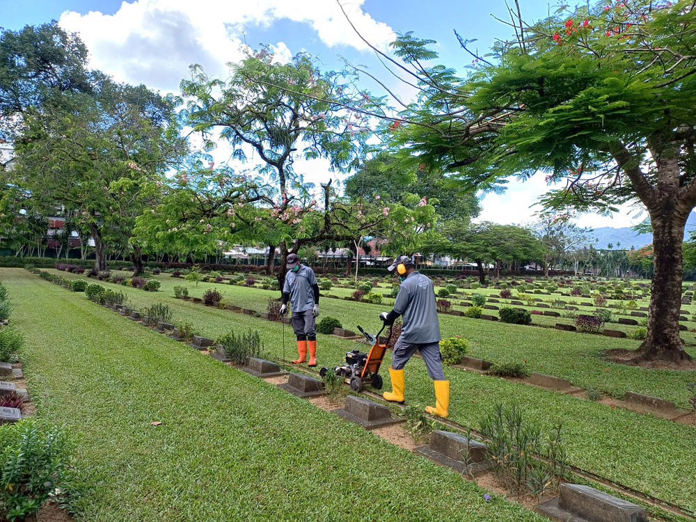 CWGC Gardeners edge borders with a handheld lawnmower.