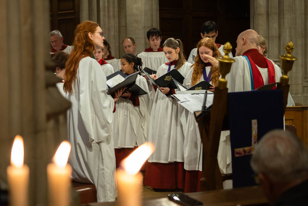 A church choir singing with candles in the foreground.