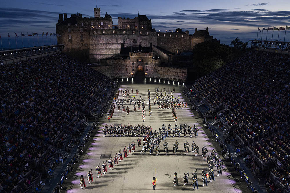 Edinburgh Military Tattoor facing Edinburgh Castle. Military figures are arrayed in formation during a parade. Two banks of stands flank the parade ground.