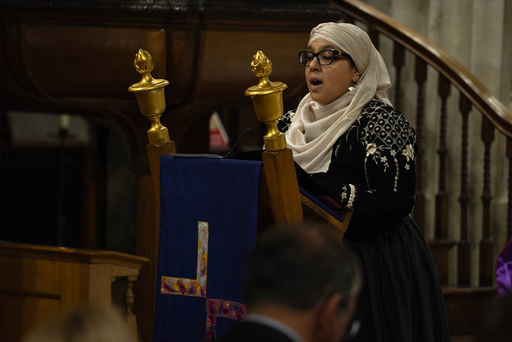 Onjali Q. Raouf gives a reading on a gold an dblue church lectern.