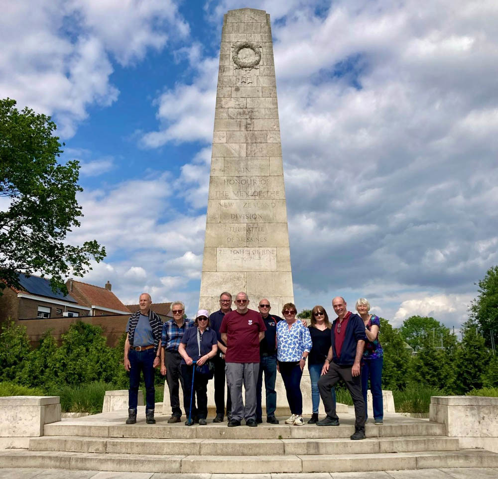 A group of volunteers pose for the camera underneath a large obelisk-like war memorial,