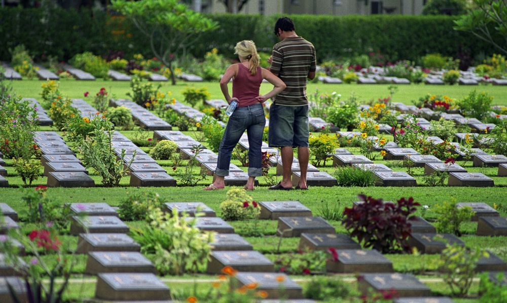 Two visitors looking at the bronze grave markers at Kanchanburi War Cemetery.