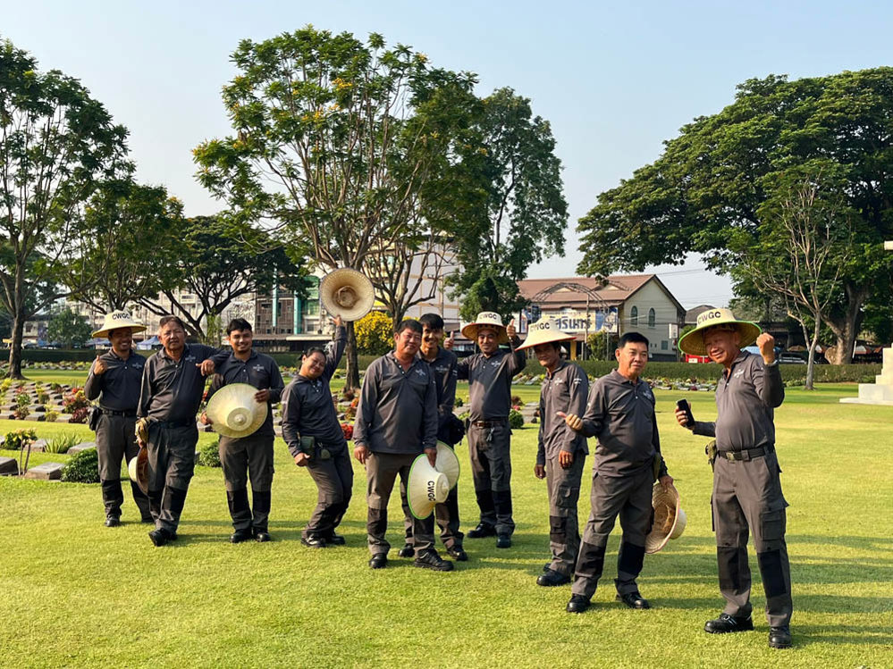 Gardeners at CWGC Kanchanaburi War Cemeter posing and waving their hats.